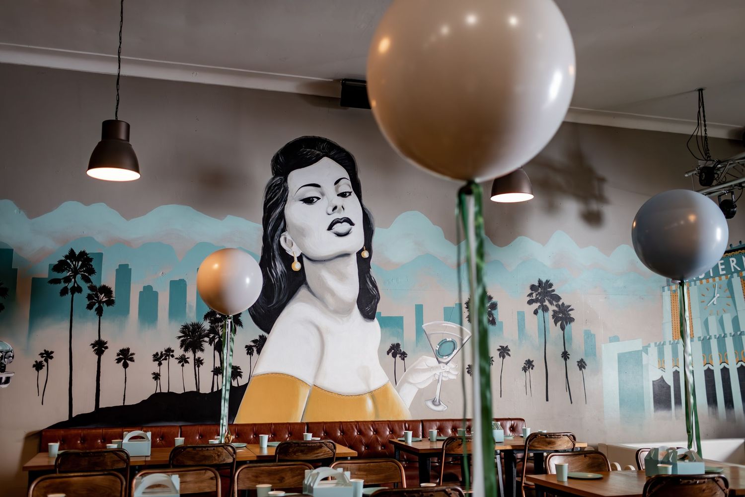 Vintage-themed restaurant interior with palm tree murals, balloon decorations, and retro artwork.