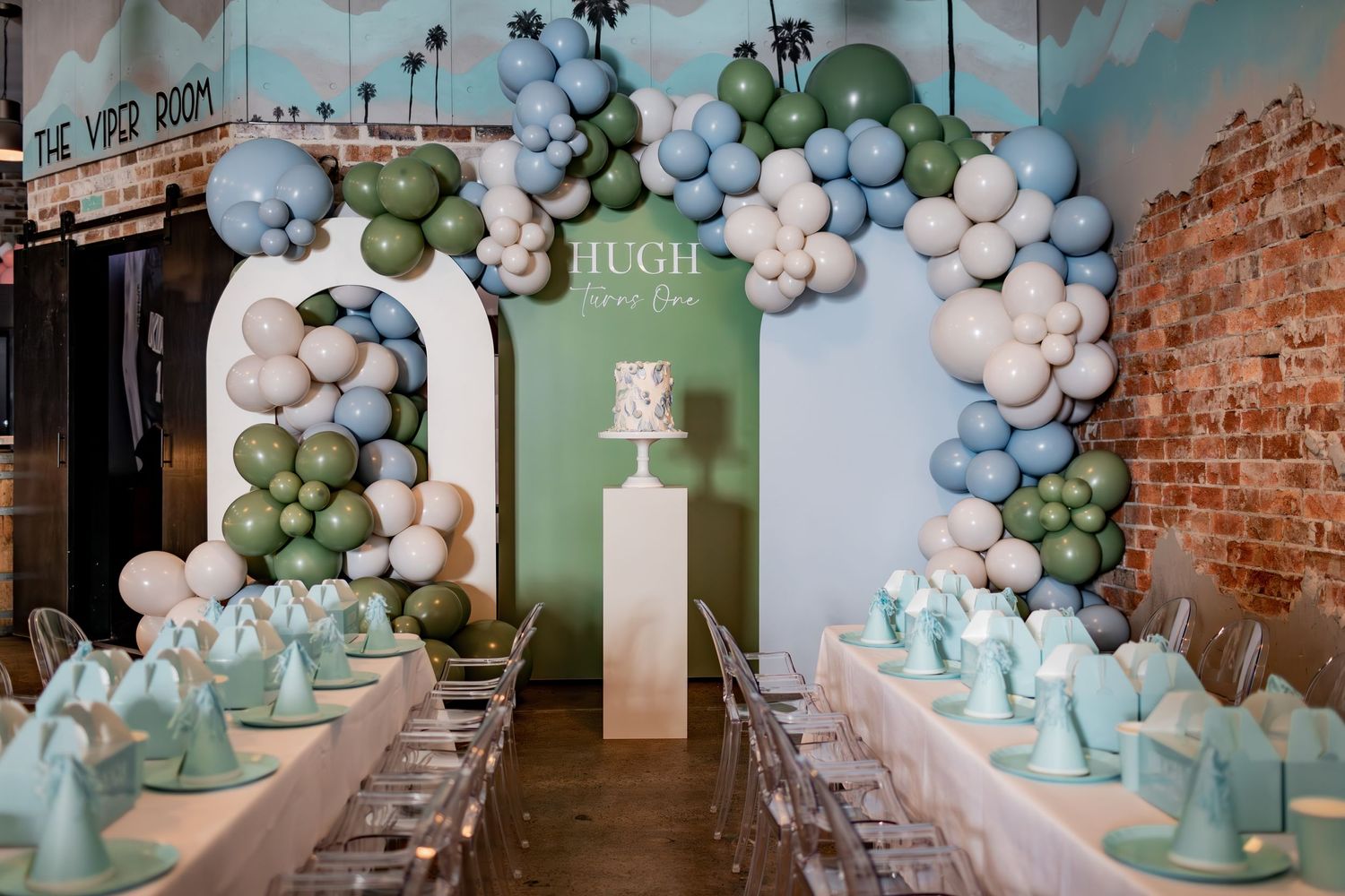 Elegant party setup with balloon arch, mint table settings and exposed brick wall.