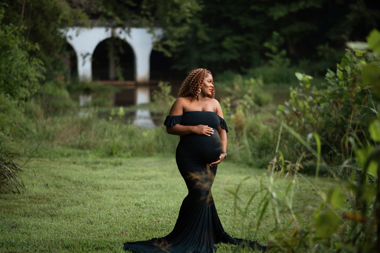 Outdoor maternity photography in black dress among natural garden setting.