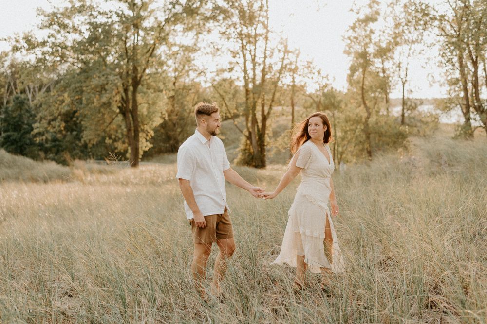 Romantic couple standing in a golden field at sunset holding hands and looking at each other.