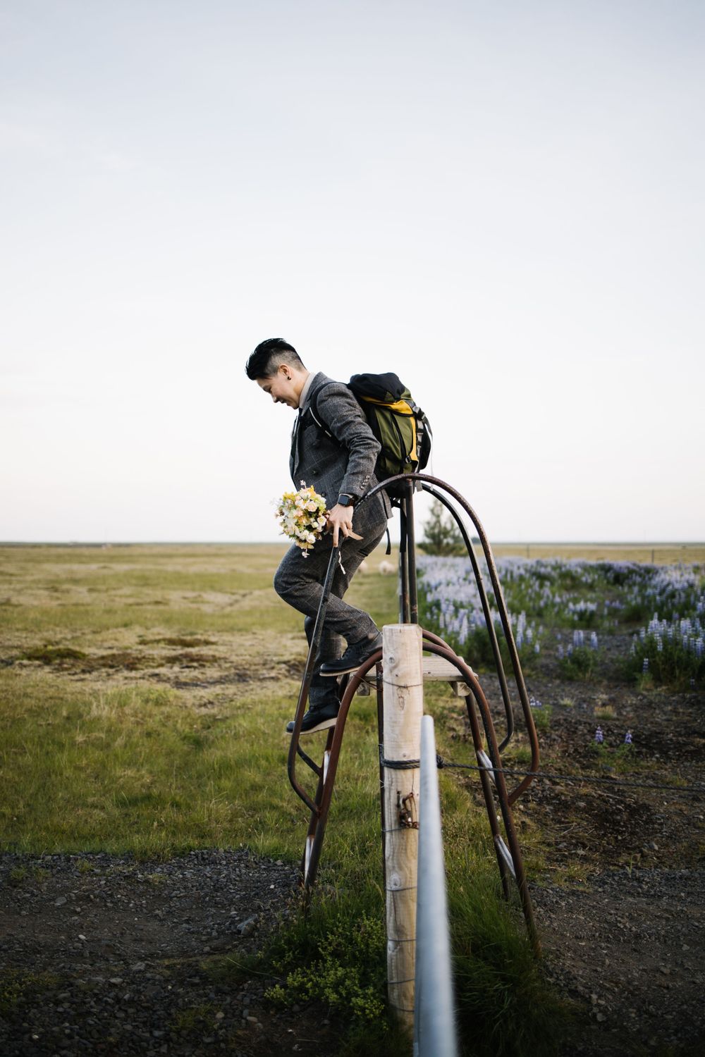 A person in formal attire climbs on metal railings against a misty natural landscape.