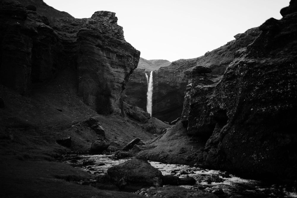 Dramatic black and white landscape of waterfall flowing through rocky canyon.