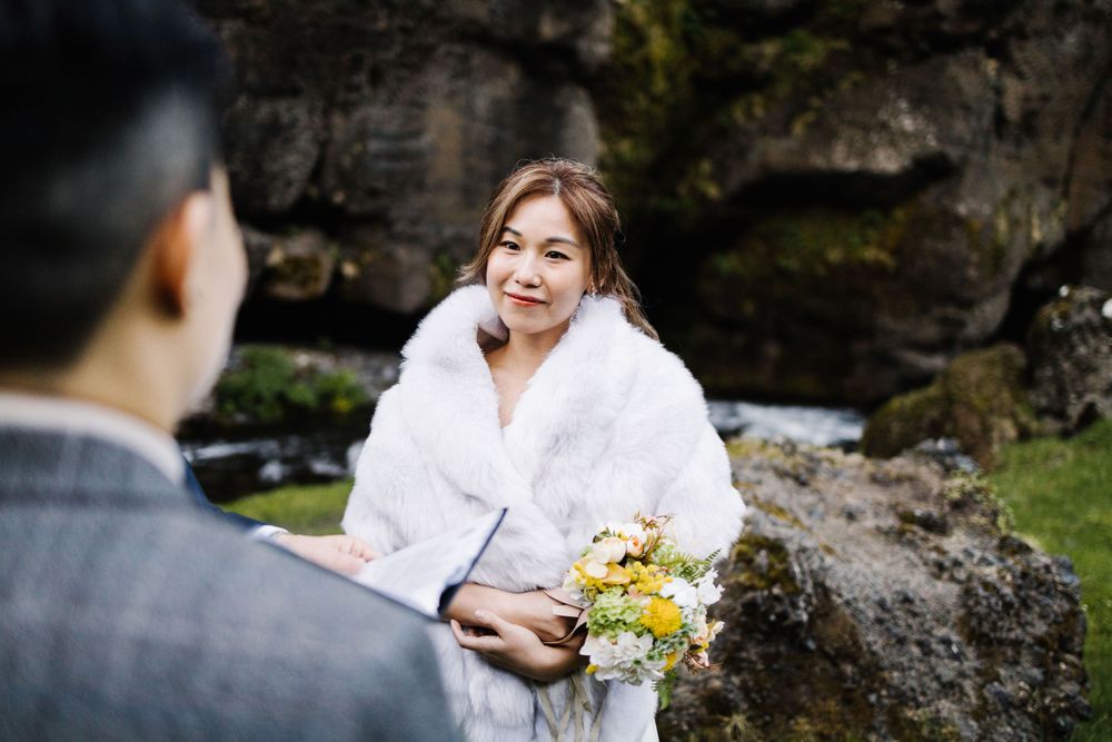 Outdoor wedding moment against rocky cliff backdrop with white fur shawl and yellow bouquet.