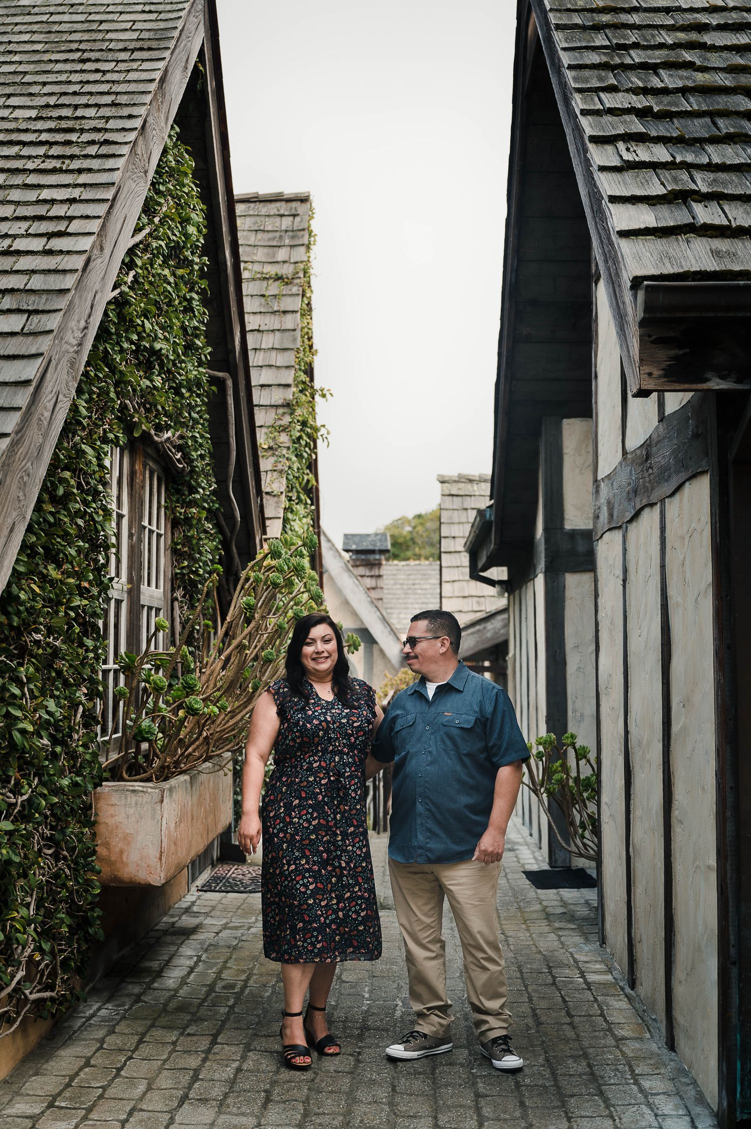 A couple stands in a charming alleyway between ivy-covered buildings.