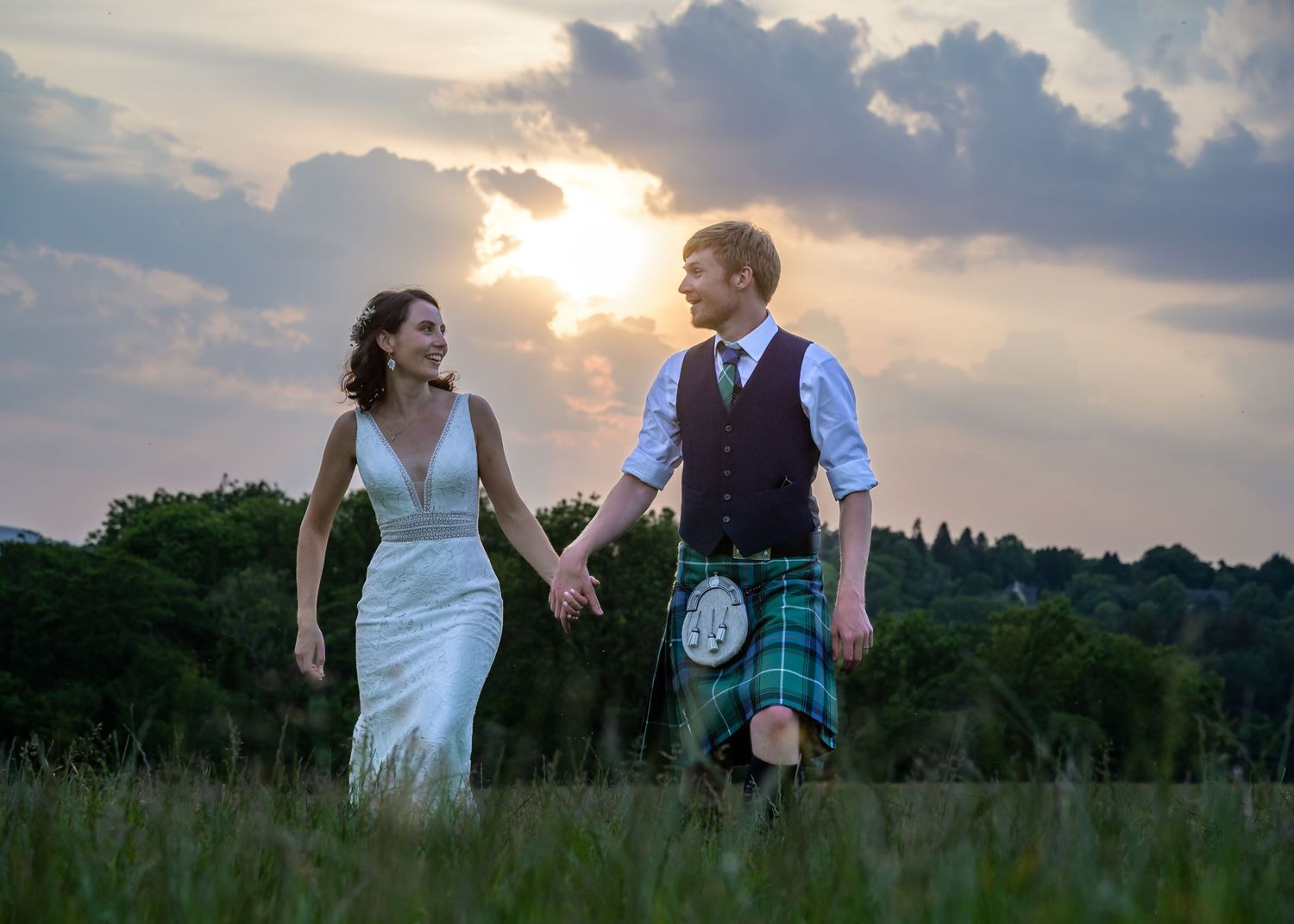 Bride and groom walking in field at sunset in Scotland