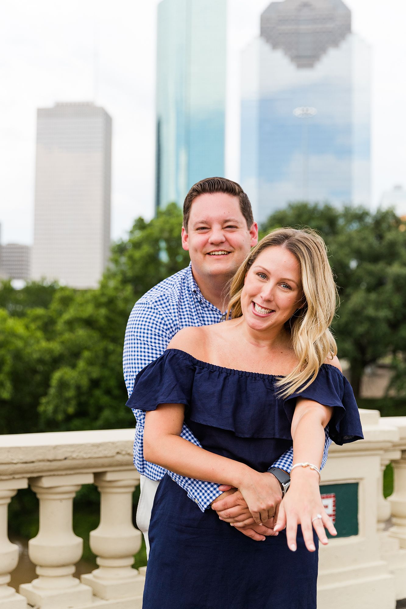 Couple embracing on balcony with urban skyline visible in background.