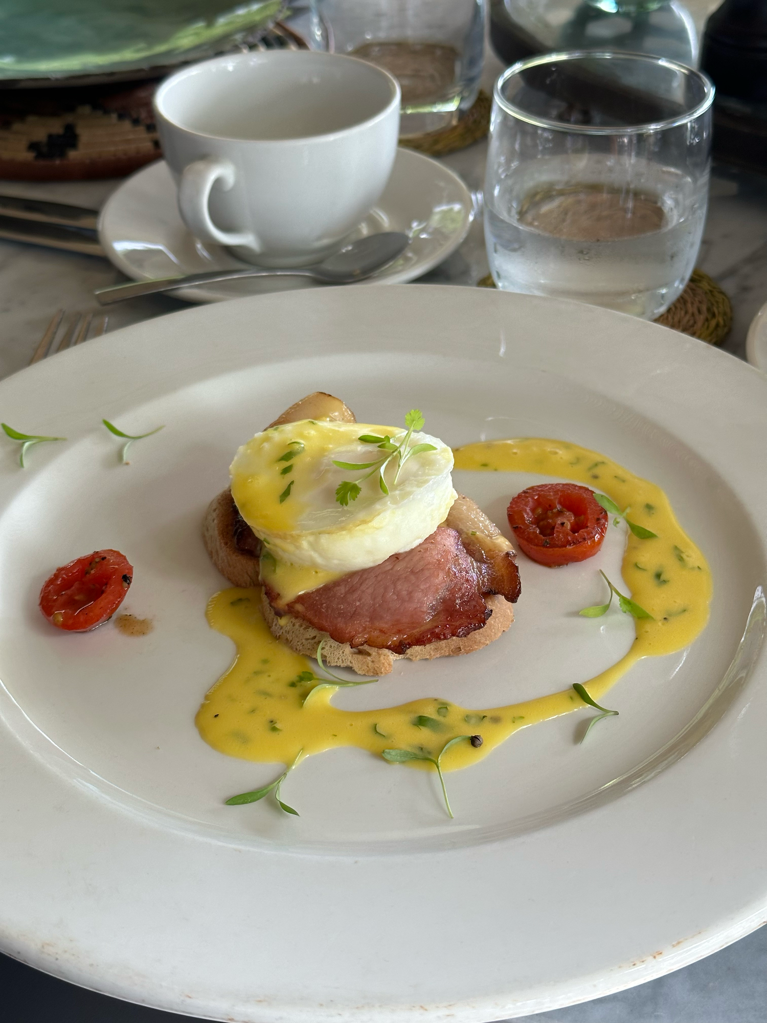 Eggs Benedict with ham served on a white plate with hollandaise sauce and roasted cherry tomatoes.