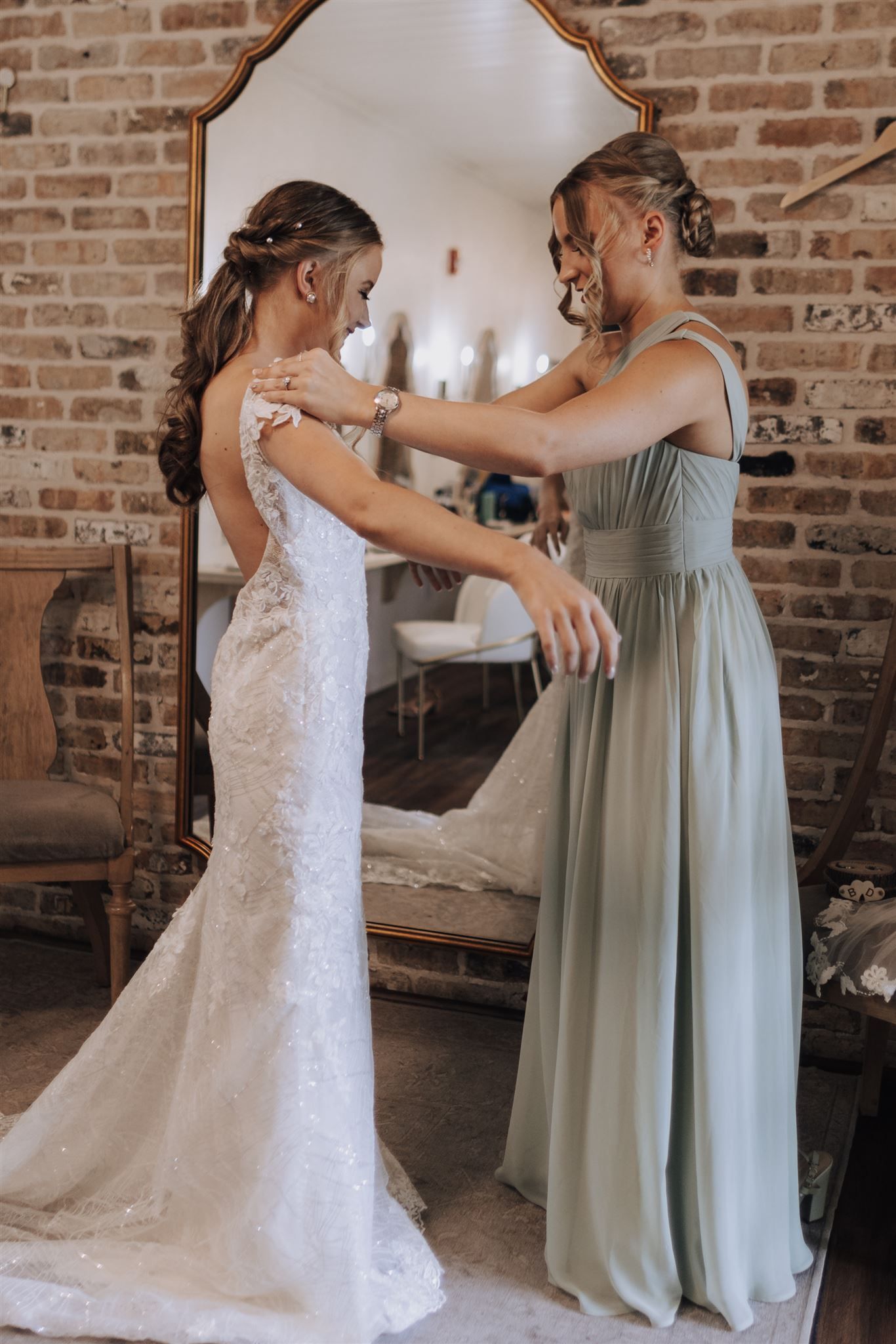 Emotional wedding dress fitting moment with bridesmaid in sage green gown.
