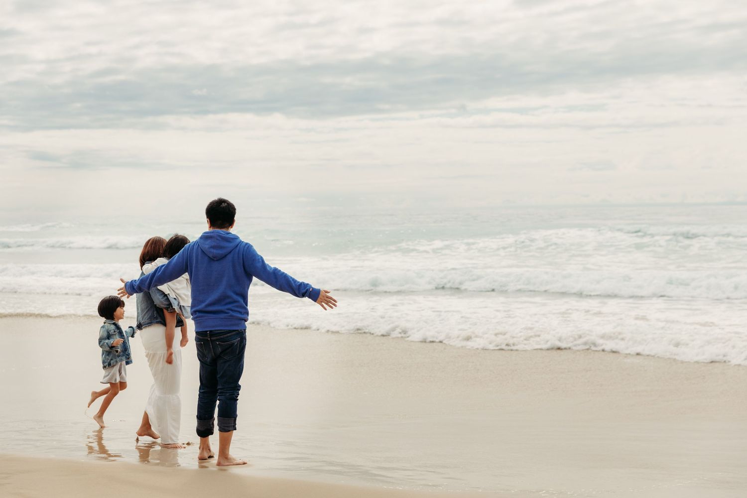 Family walking together holding hands on beach at sunset creating playful moment.