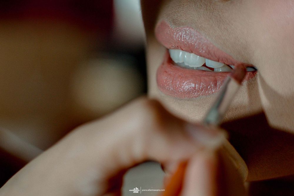 Close-up shot of lips being carefully applied with makeup during wedding preparation.