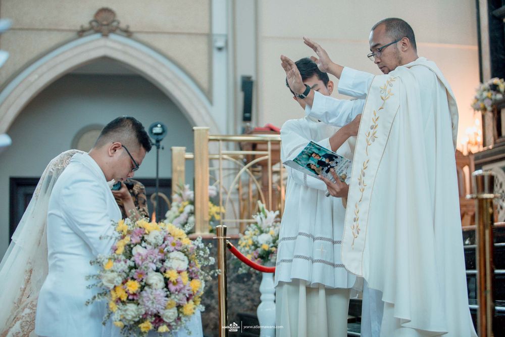A clergy member performs a blessing during an outdoor wedding ceremony with floral decorations.