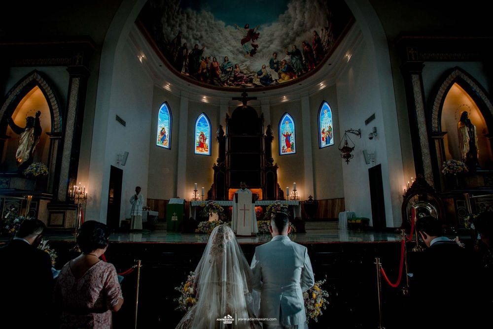 A couple stands at the altar of a grand cathedral with stained glass windows and ornate decorations during their wedding ceremony.