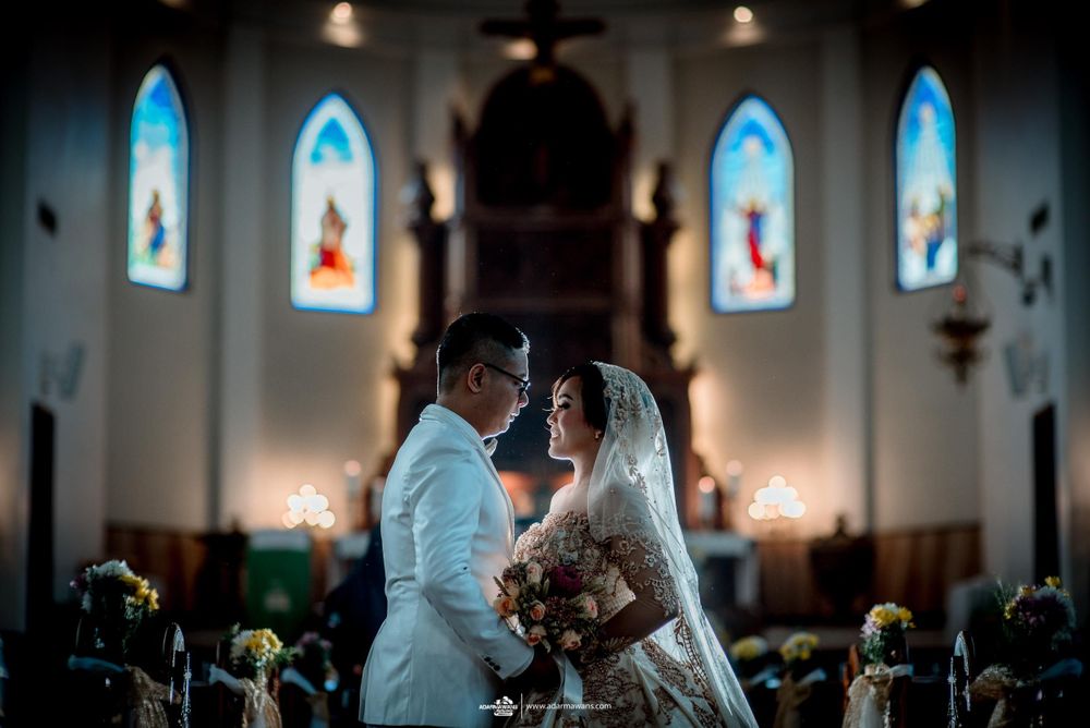 An intimate wedding moment captured in a church with illuminated stained glass windows in the background.
