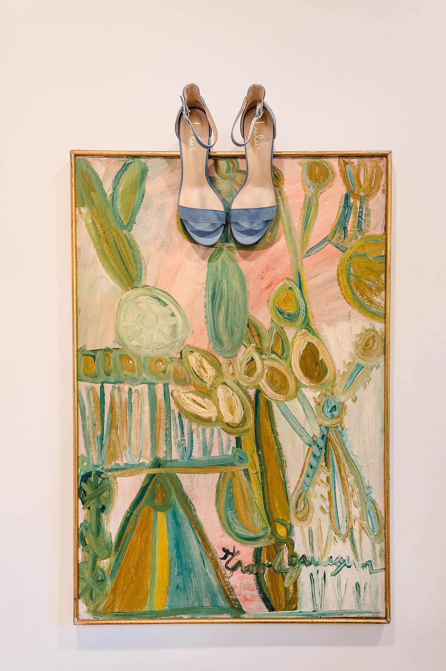 Blue wedding shoes displayed on abstract floral artwork with green and peach tones.