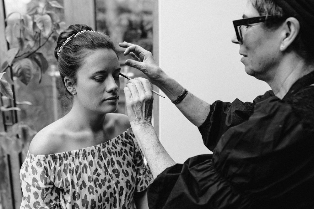 Professional makeup artist applies cosmetics to a client wearing a leopard print top during wedding preparations.