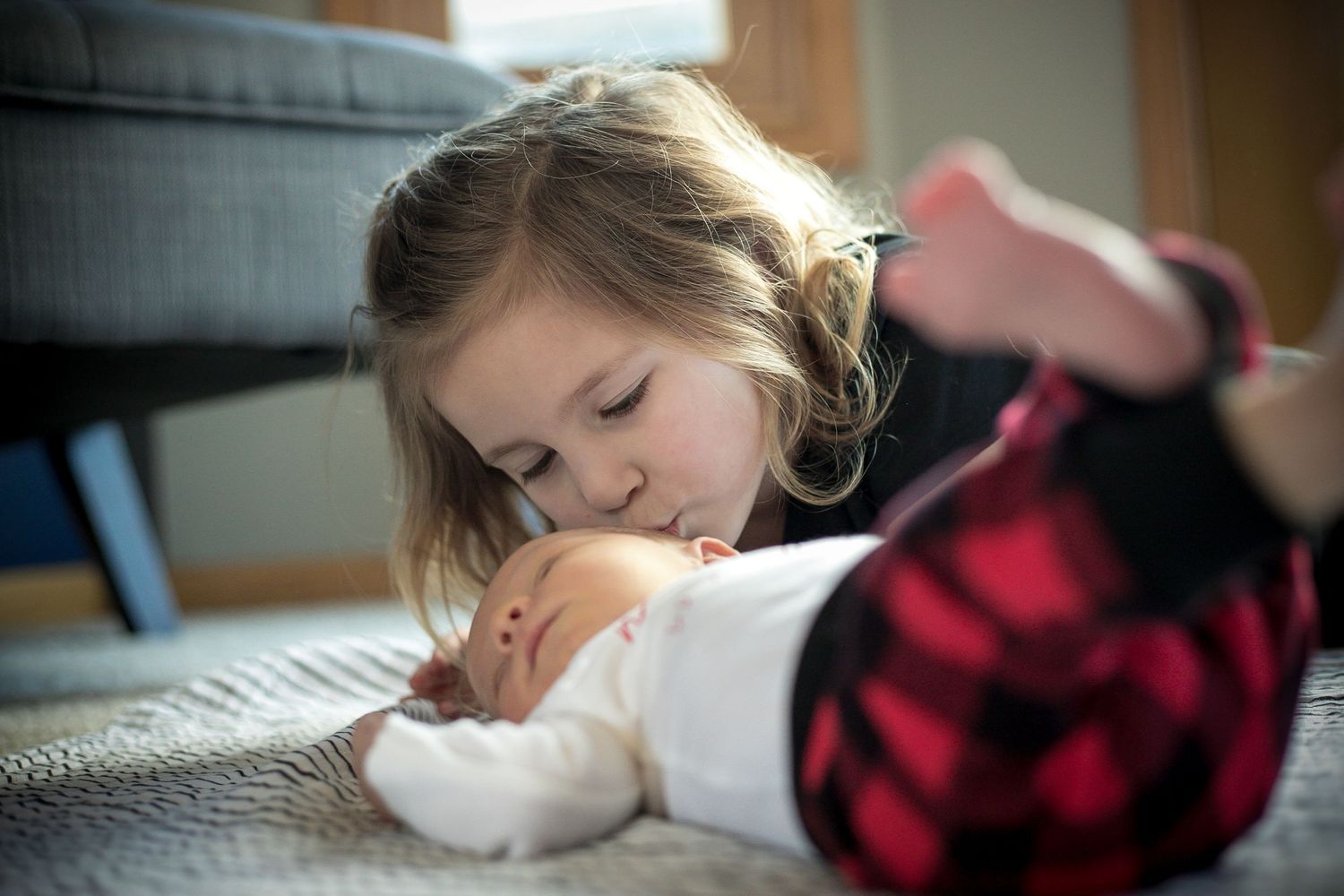 Big sister giving her new baby brother while he is laying on the floor in the home during their fresh 48 session.