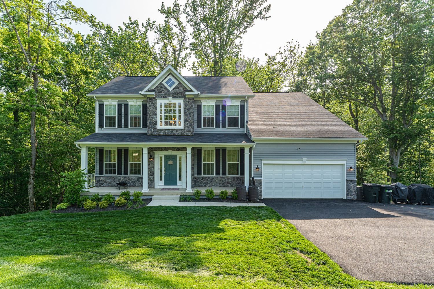 Modern colonial style home with attached garage nestled among trees on landscaped property.