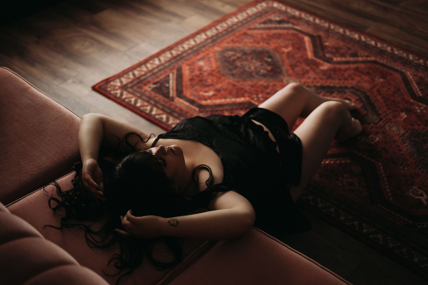 Sensual boudoir photo on couch with vintage Persian rug in warm lighting.