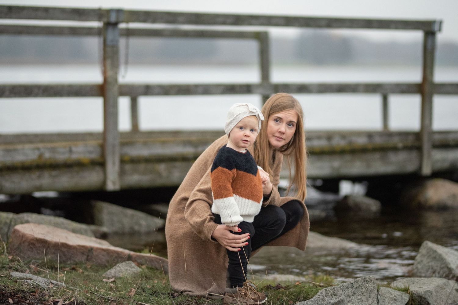 Parent and child sharing a moment on wooden dock by water.