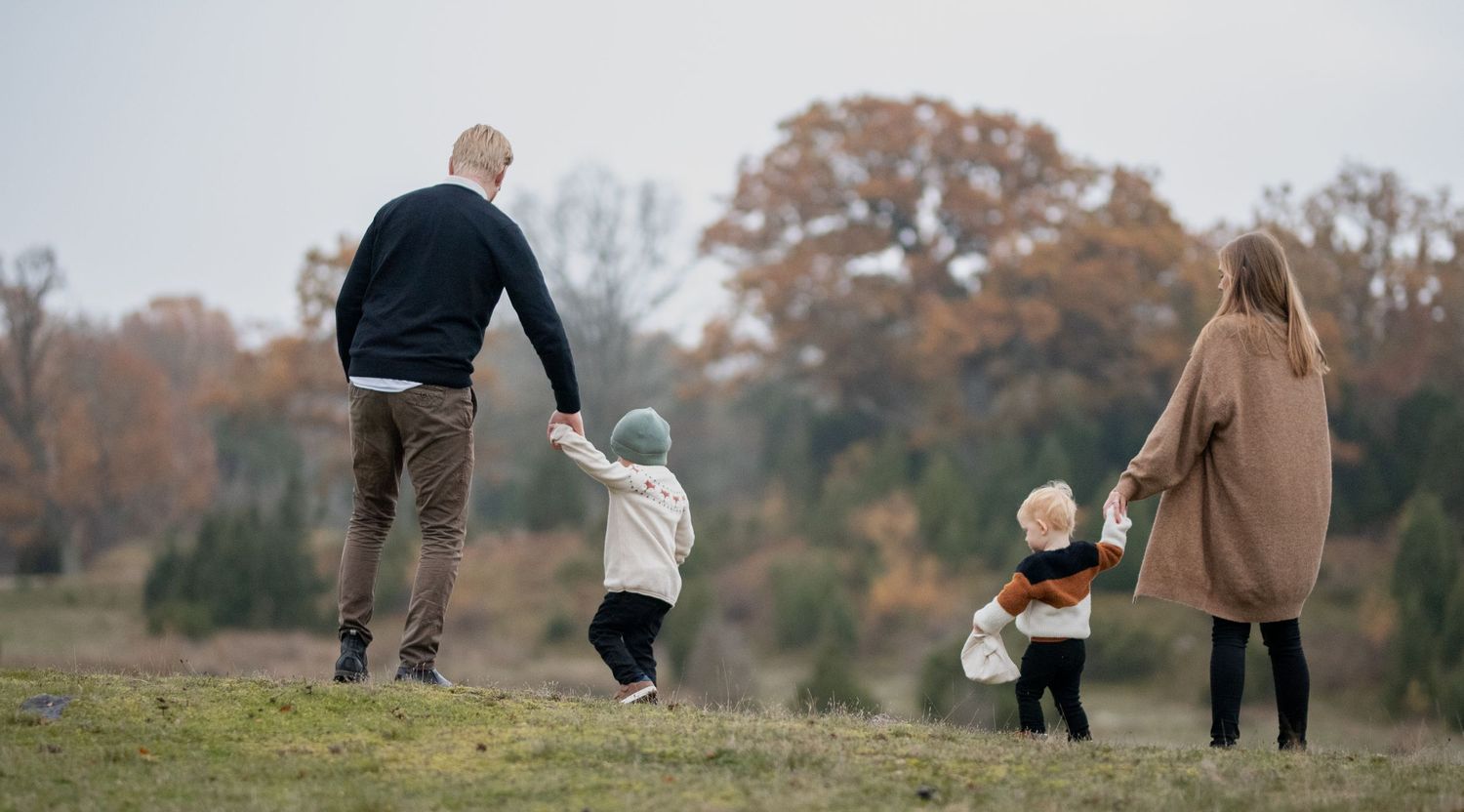 Family walking together on grassy hill during autumn afternoon.