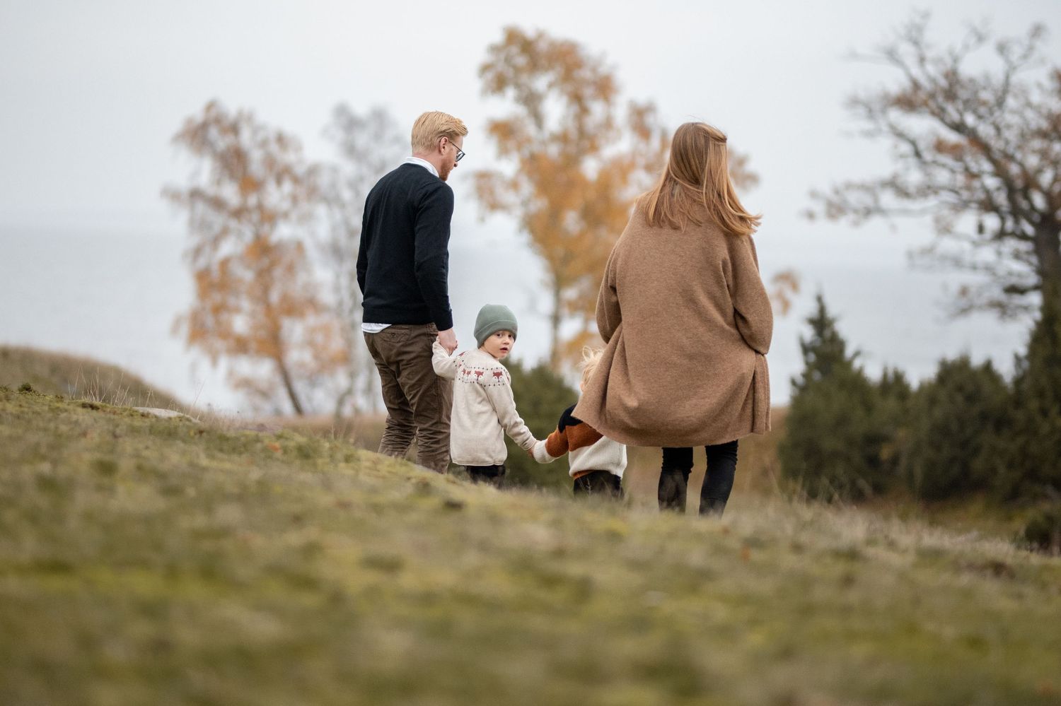 A family walks together on a grassy hill during autumn with trees in the background.