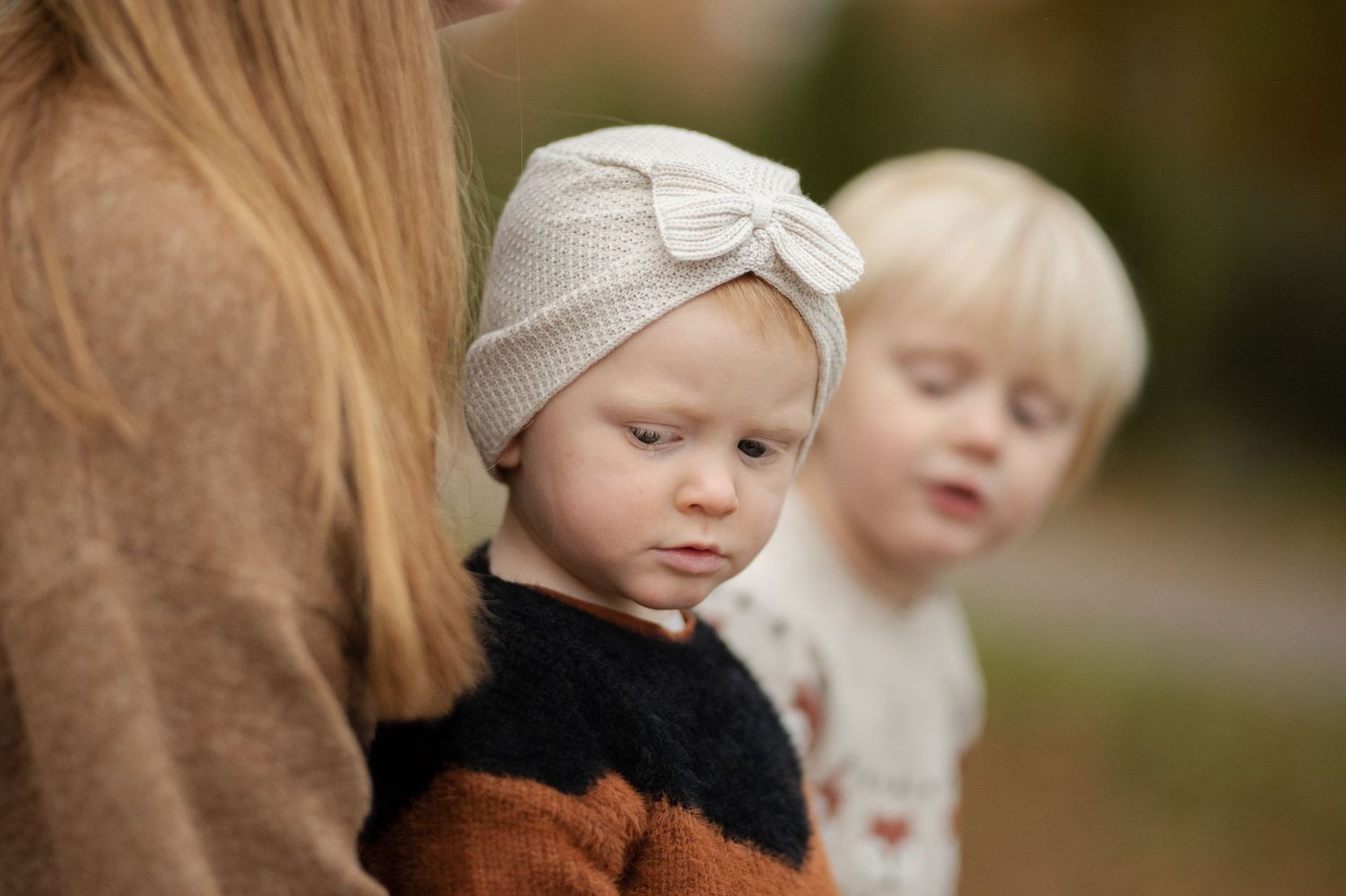 Small children in winter attire stand close to an adult wearing a brown coat.