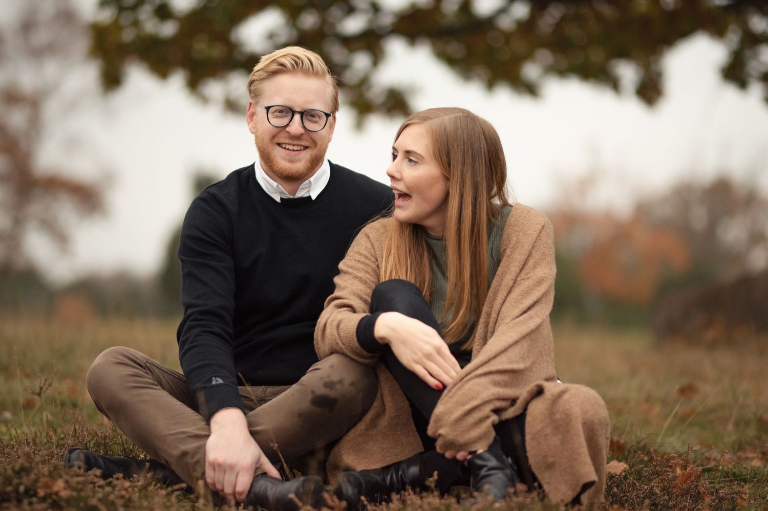 Couple sitting on ground wearing coordinated fall outfits in an autumn setting.