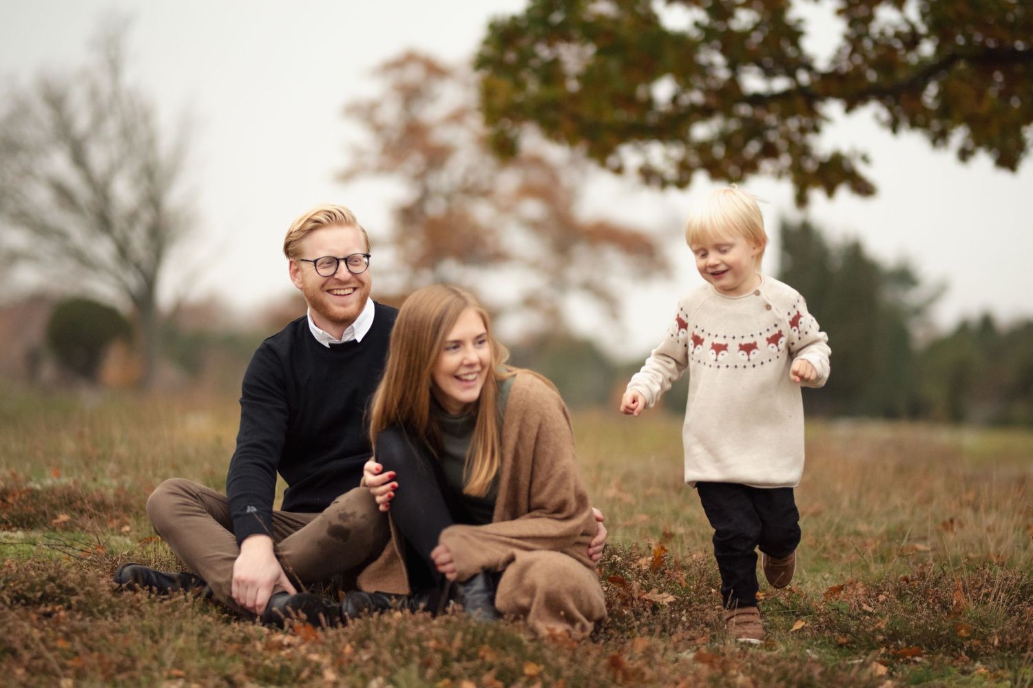 Family enjoying a playful moment together on autumn grass under a tree.
