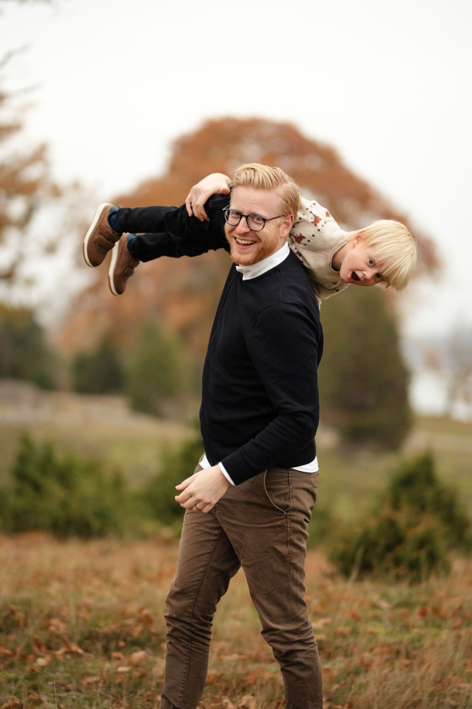 Playful moment captured outdoors with person carrying child horizontally in autumn setting.