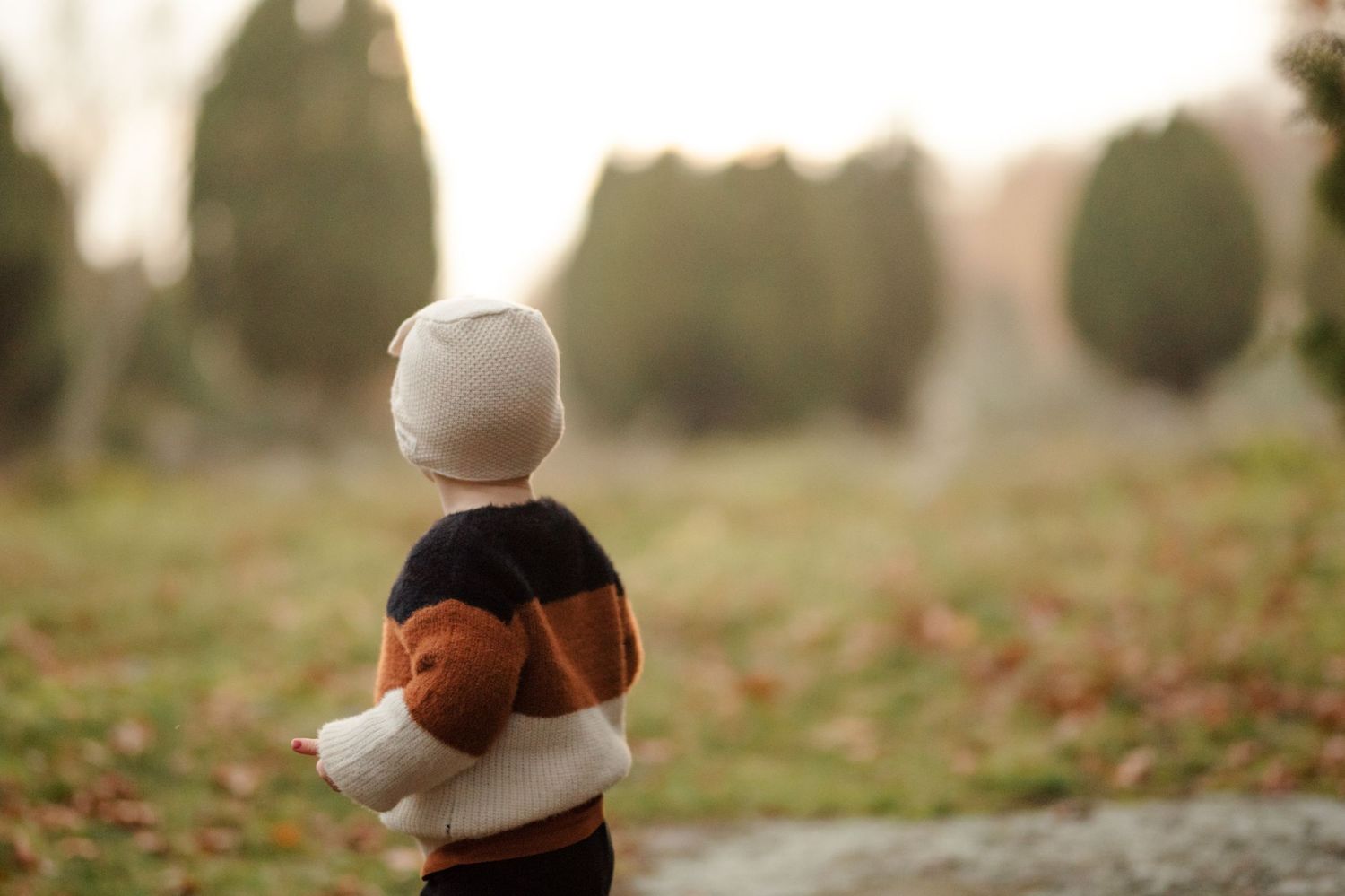 Small figure in warm clothing stands amid fallen autumn leaves at dusk.
