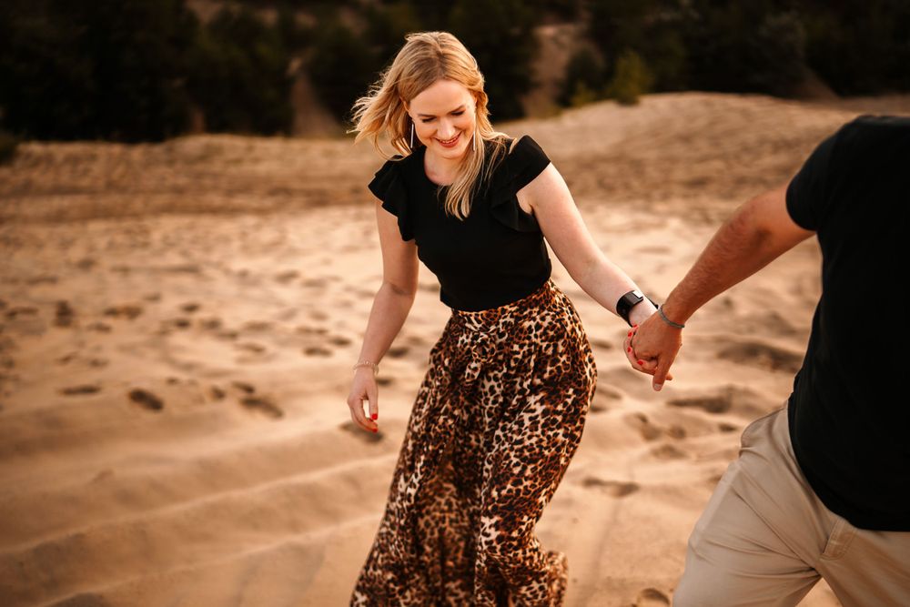 Couple walking hand in hand on sandy dunes at sunset.