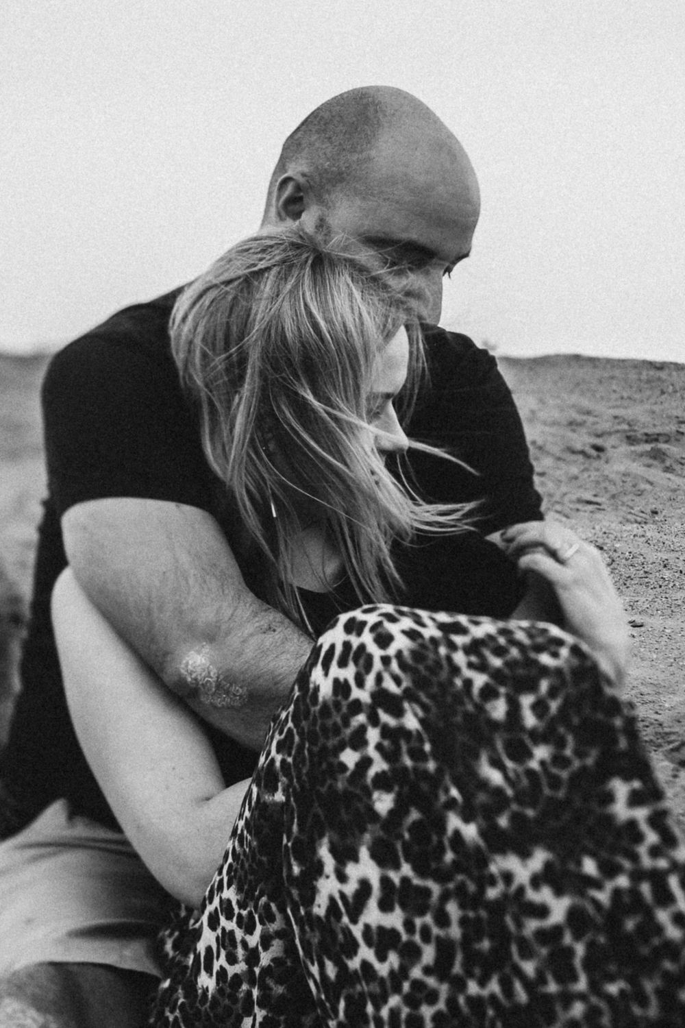 Black and white intimate portrait of couple embracing on desert landscape.