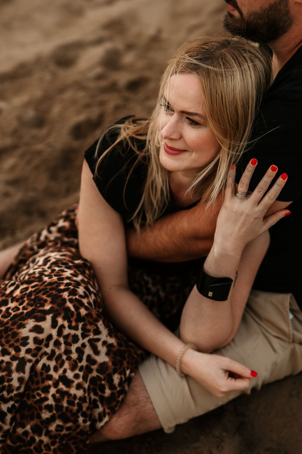 Romantic couple cuddling on beach sand wearing leopard print dress and casual clothes.