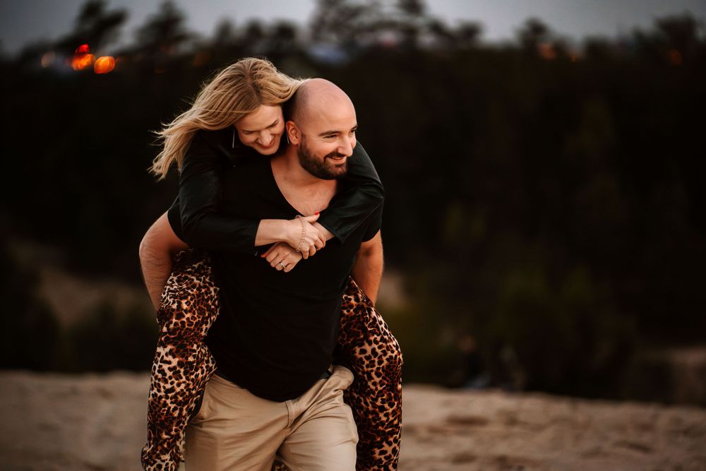 A playful piggyback ride moment captured on a sandy beach at dusk.