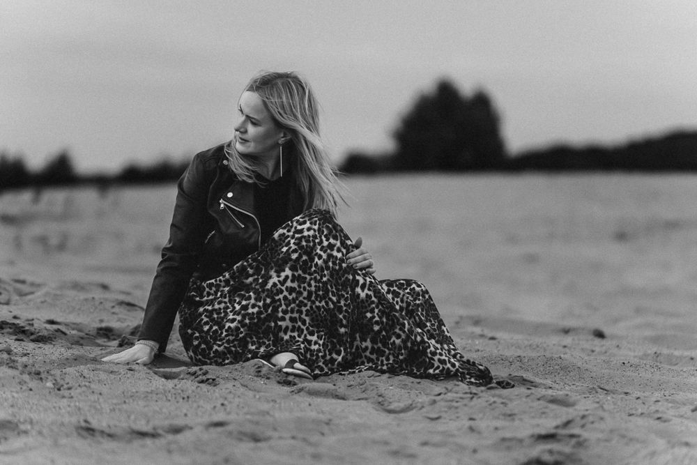 Black and white portrait of person in leopard print dress sitting on beach.