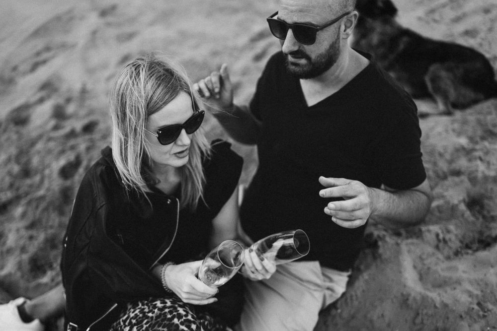 Black and white photo of couple wearing sunglasses and sharing snacks outdoors.