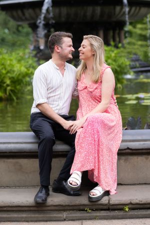 Newly engaged couple sits laughing together at Bethesda Fountain, Central Park.
