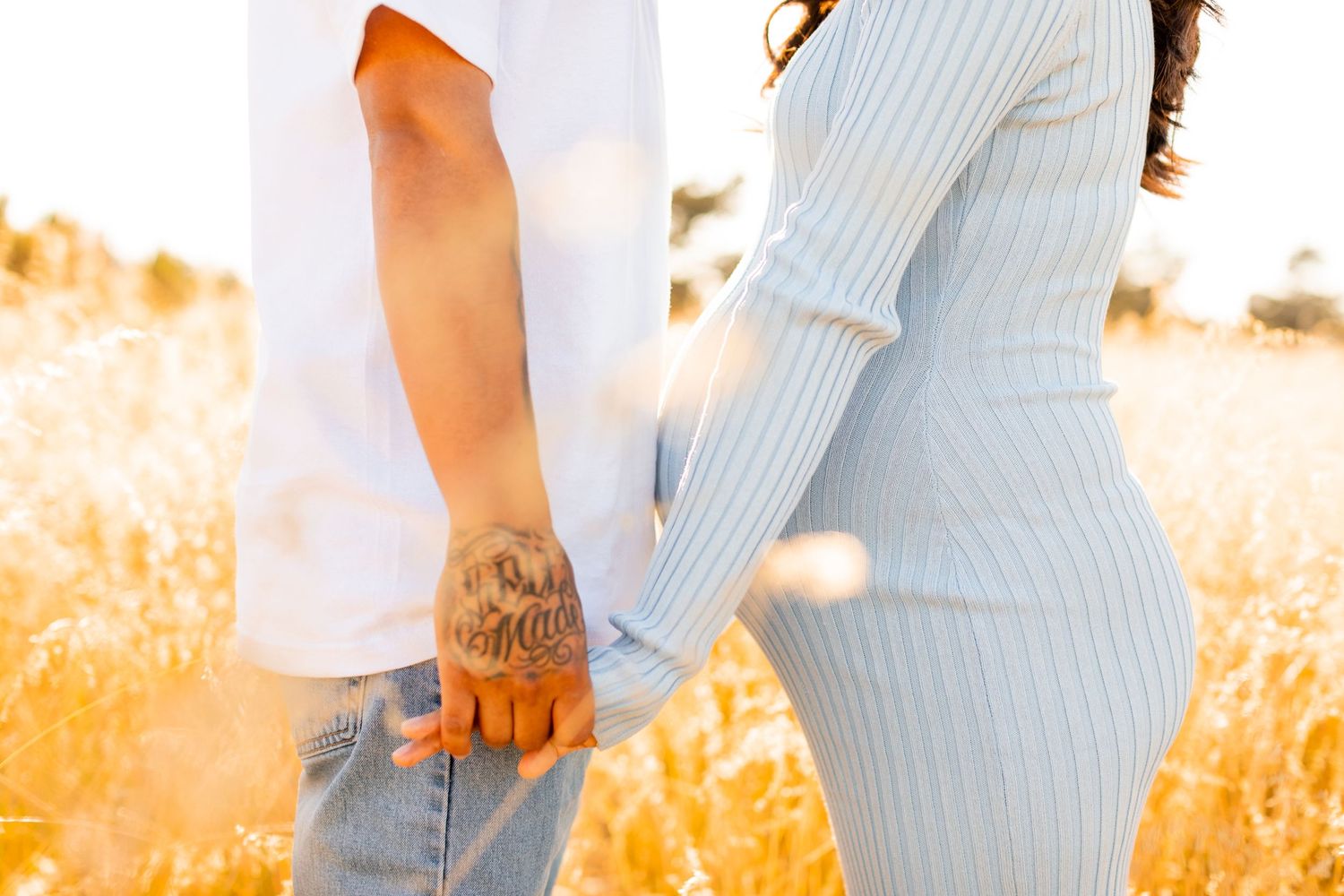 Close-up of couple holding hands in golden field, showing tattoo on one person's wrist.