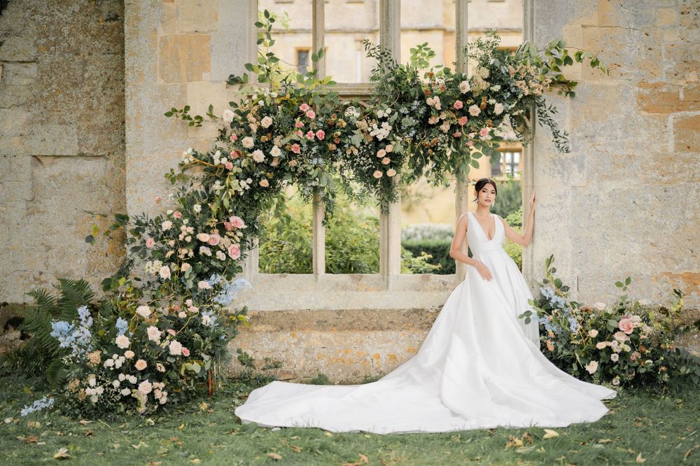 Wedding gowns showcased against stone wall with climbing roses and gothic windows.