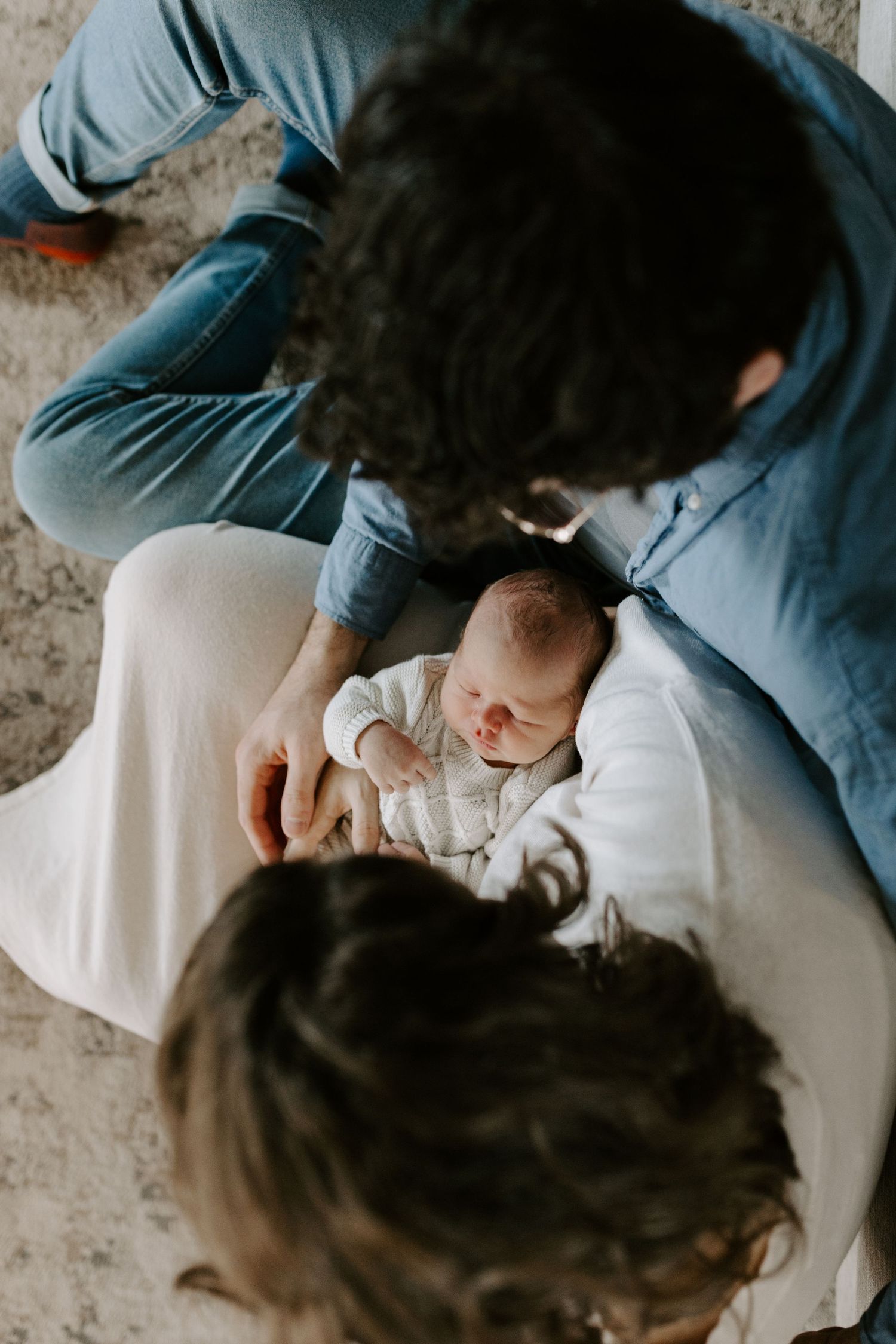 New parents gaze lovingly at their sleeping newborn baby from above in a tender indoor moment.