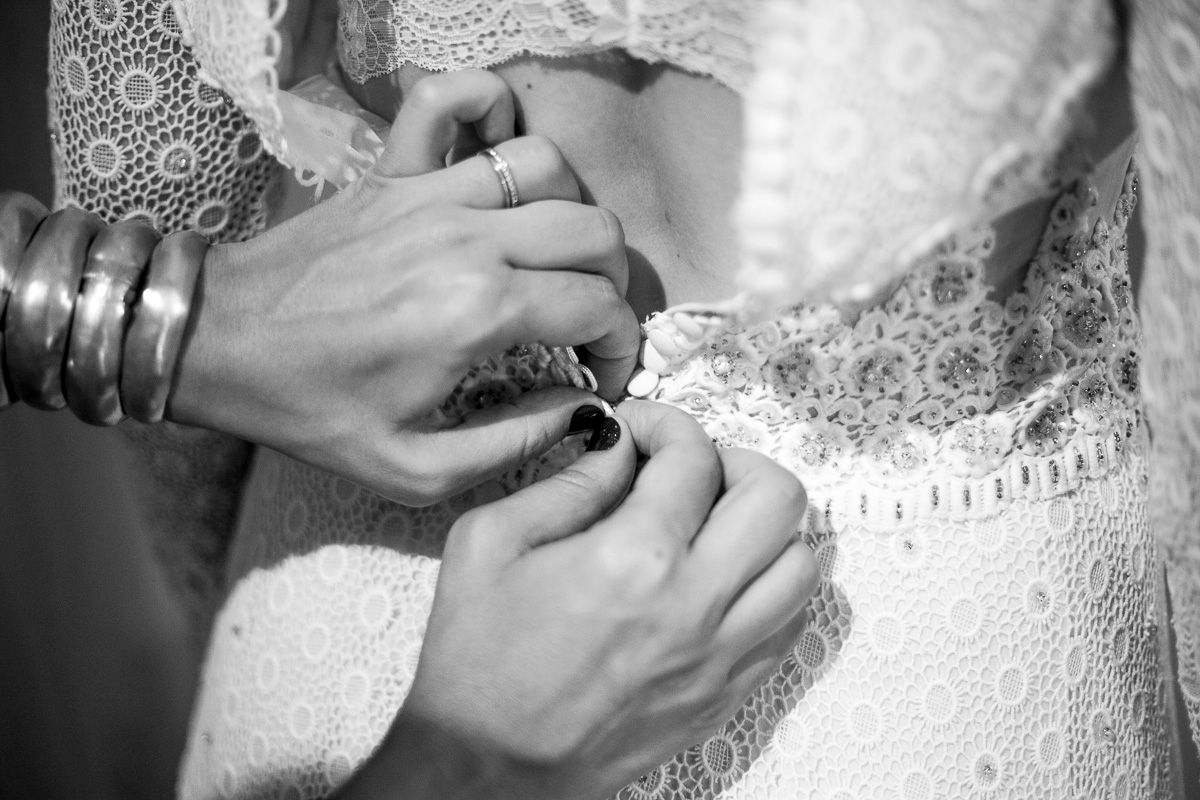 Close-up black and white photo of hands adjusting details on a lace wedding dress.