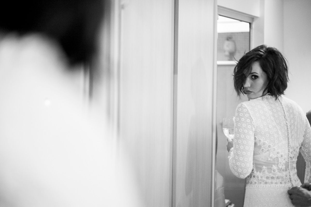 Black and white photo of someone in an elegant white dress looking in a mirror during wedding preparations.