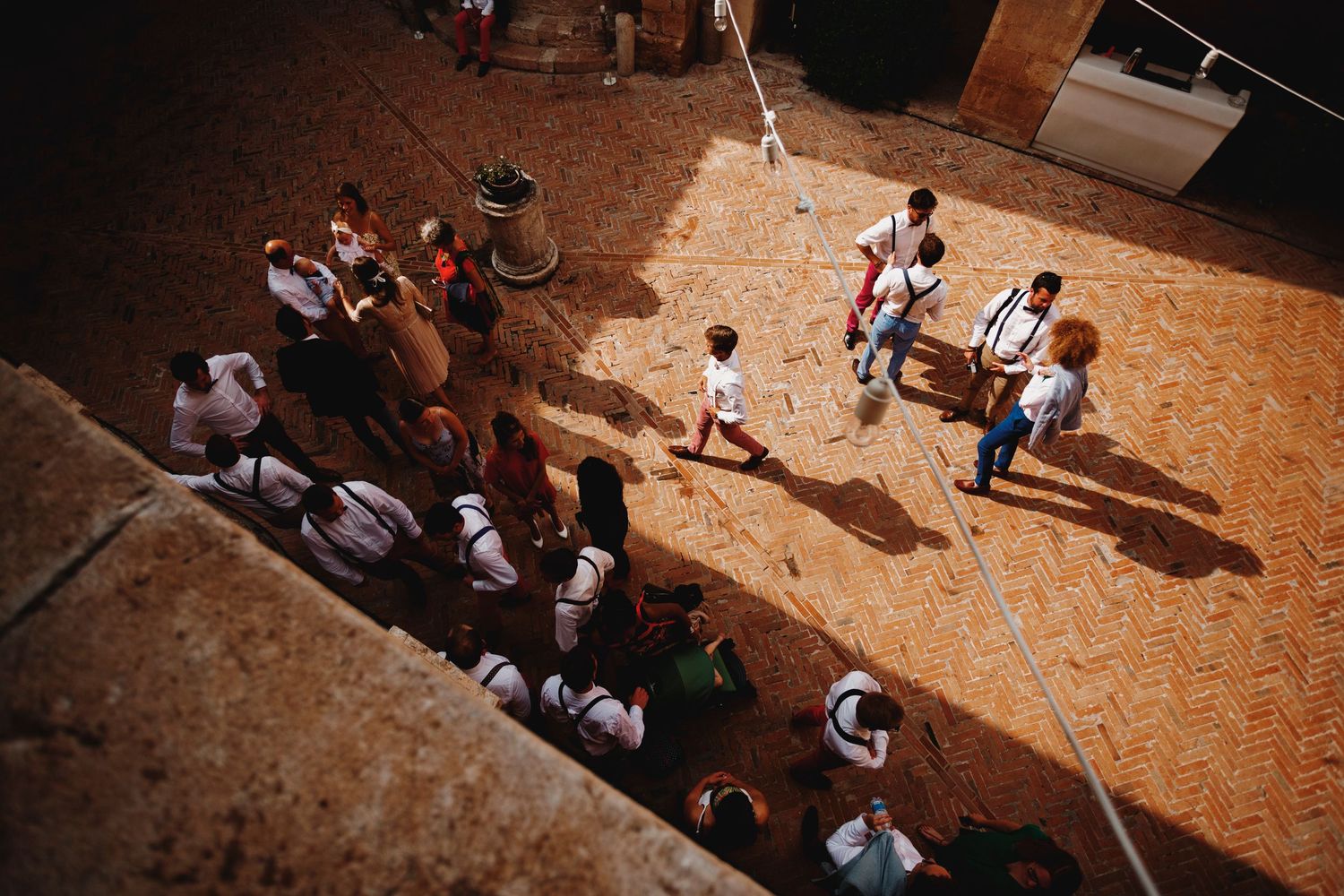Aerial view of wedding guests gathered in a rustic courtyard during daytime celebration.