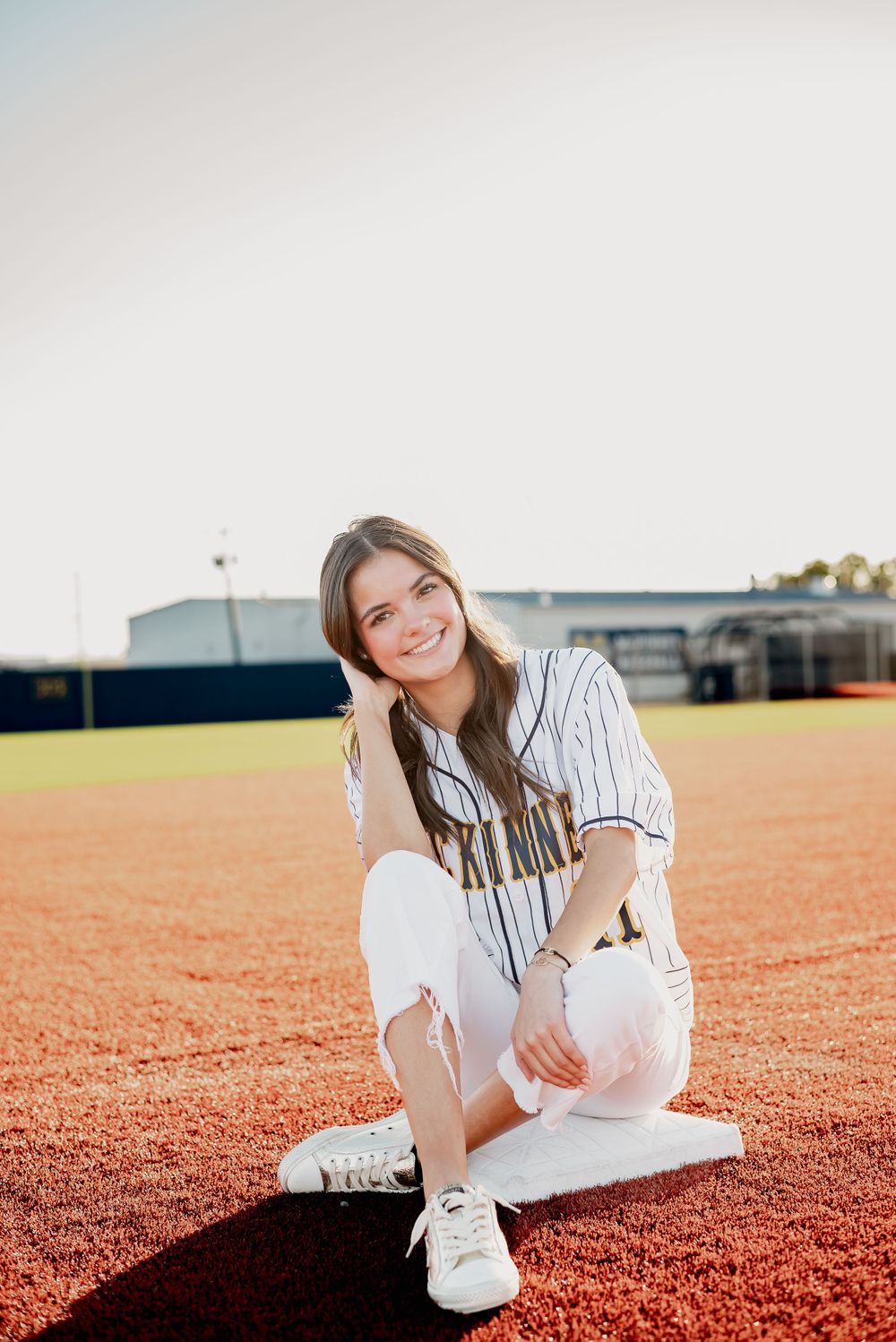 Portrait of someone in baseball attire sitting on red clay field surface.
