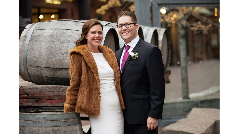 Newlyweds pose next to rustic wooden barrel in formal wedding attire.