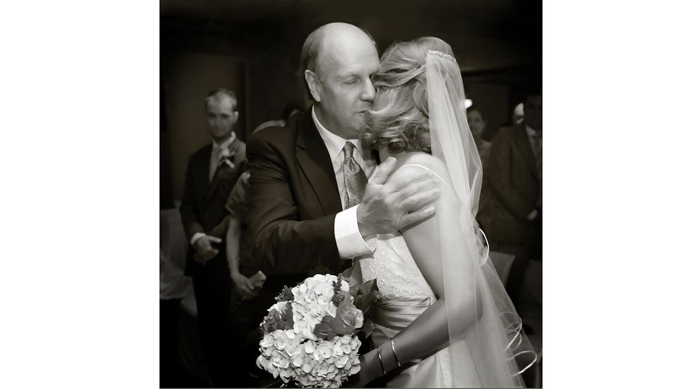 Black and white wedding photo capturing intimate dance moment with bridal bouquet.
