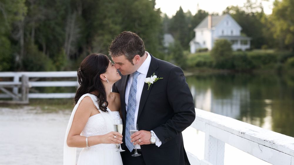 Intimate wedding portrait of couple kissing on white bridge near water.
