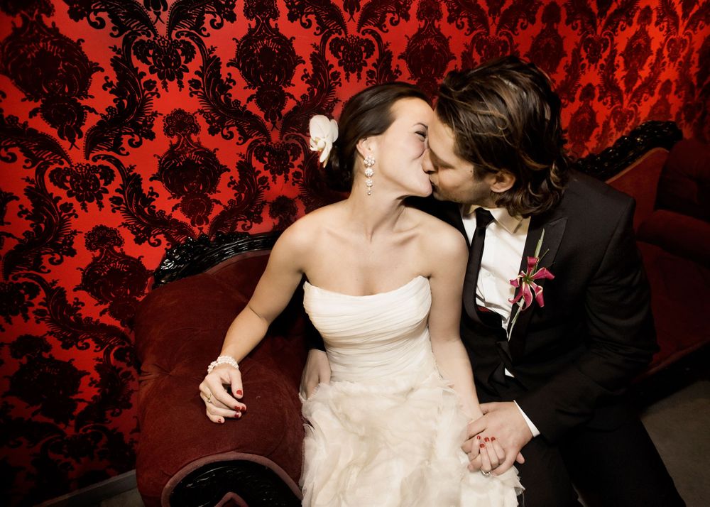 Romantic wedding moment against dramatic red damask wallpaper.