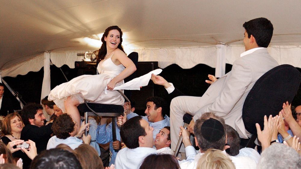 Wedding couple being lifted on chairs during lively reception celebration.