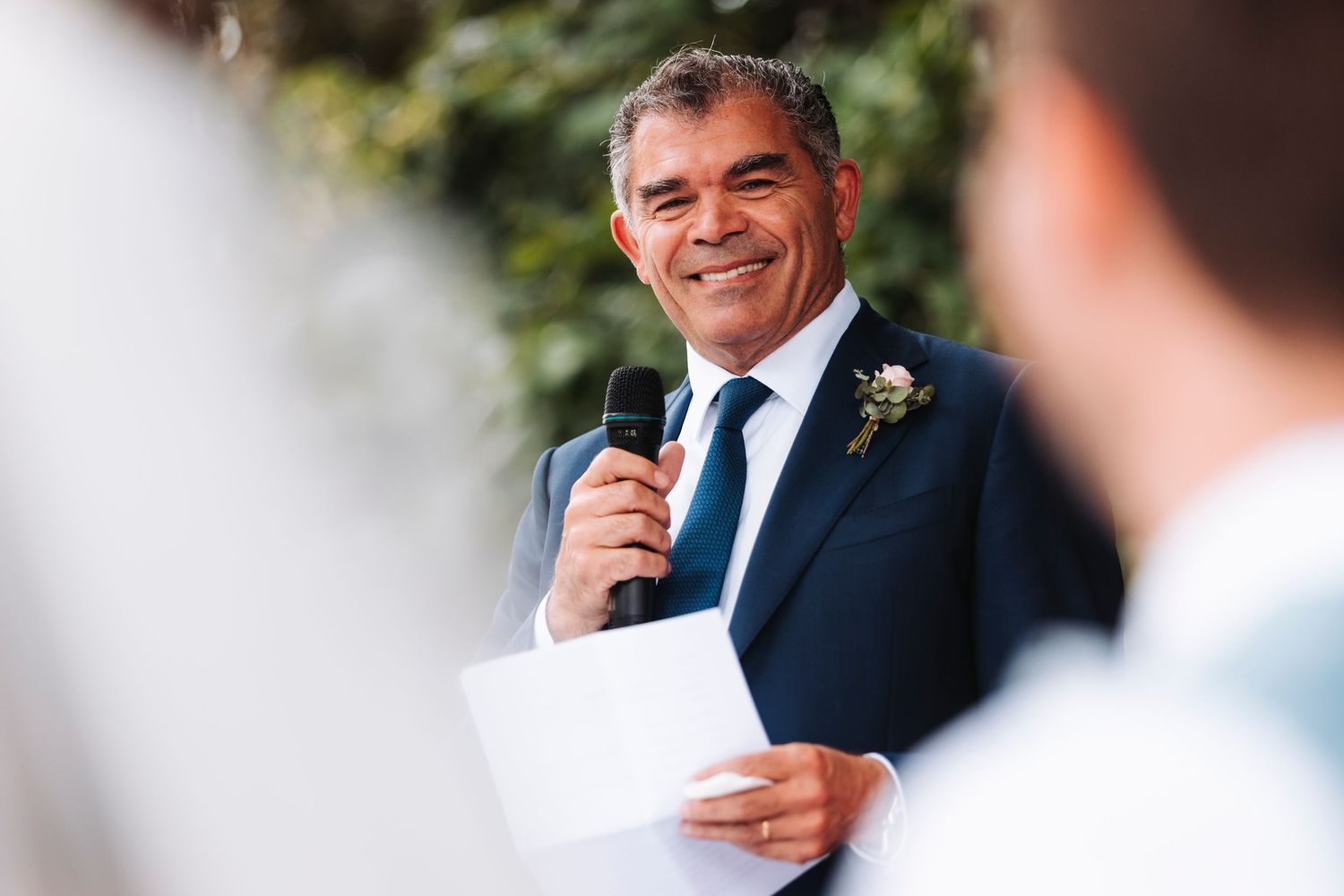 Speaker delivers wedding speech with microphone during outdoor reception.